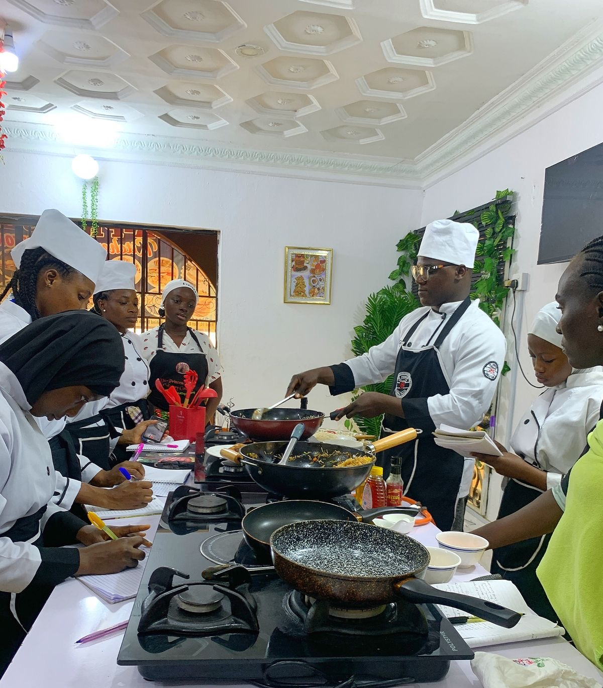 a picture of students taking notes and listening in a cooking class learning from their teacher all about cooking recipes